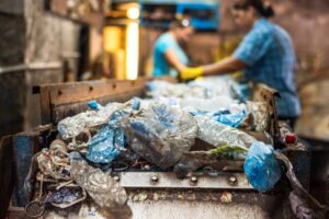 Plastic garbage on a conveyor belt at waste recycling factory. Workers on the background
