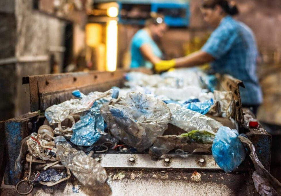 Plastic garbage on a conveyor belt at waste recycling factory. Workers on the background
