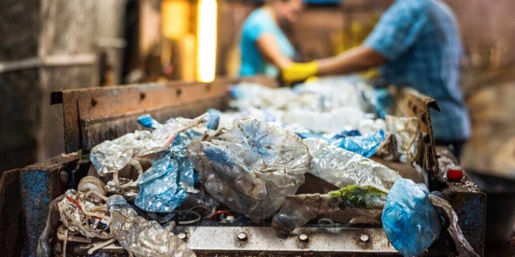 Plastic garbage on a conveyor belt at waste recycling factory. Workers on the background