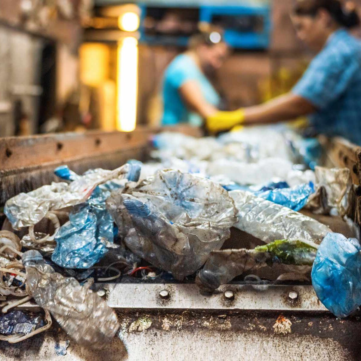 Plastic garbage on a conveyor belt at waste recycling factory. Workers on the background